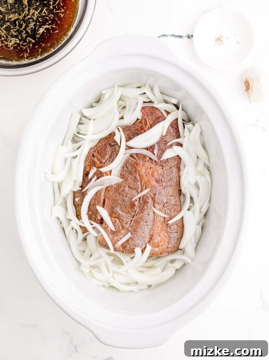 Effortless Slow Cooker French Dip Perfection 6 A large beef roast and thinly sliced onions are nestled together inside a slow cooker, ready for the flavorful braising liquid.