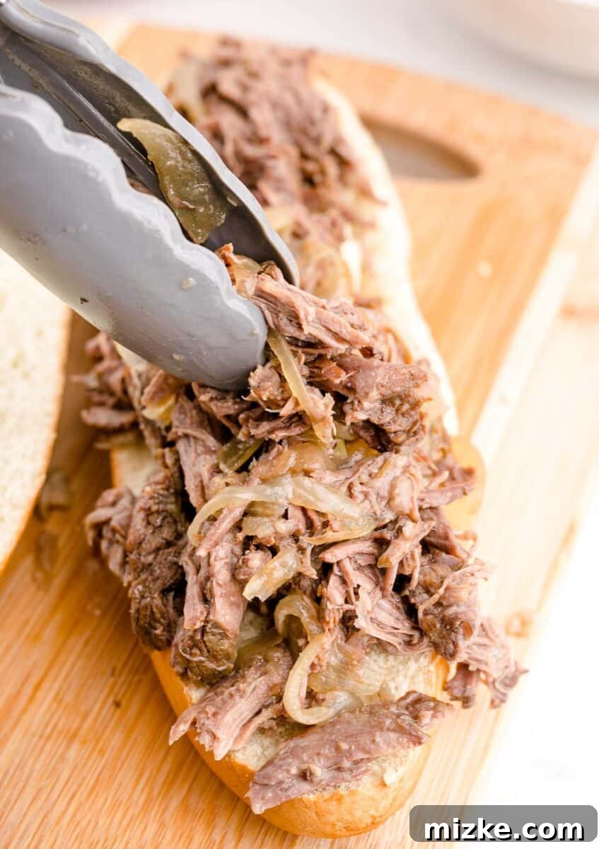Effortless Slow Cooker French Dip Perfection 8 Expertly shredded beef is generously piled onto a freshly sliced hoagie bun, preparing for the final assembly of a French Dip sandwich.