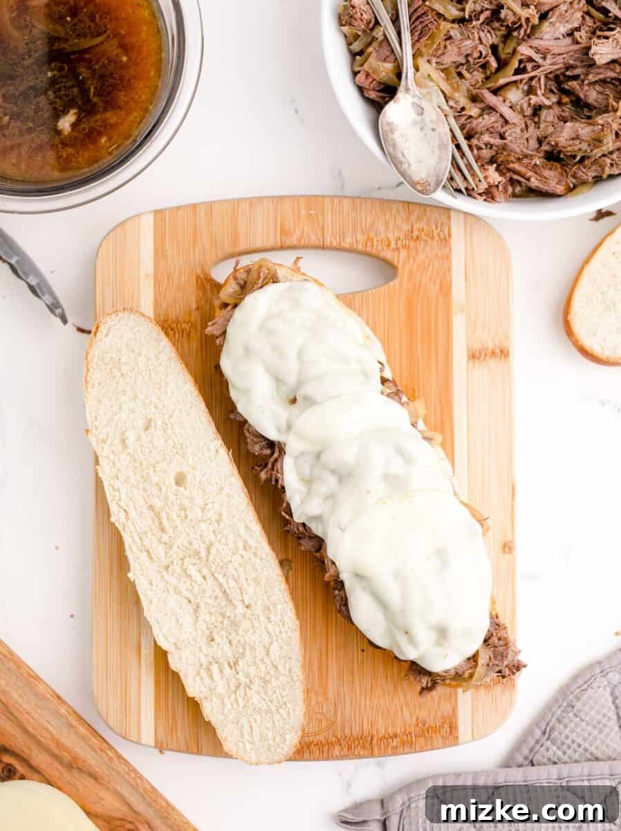 Effortless Slow Cooker French Dip Perfection 9 A perfectly assembled French Dip sandwich, toasted with melted provolone cheese, is cut in half to reveal its tender beef and onions.