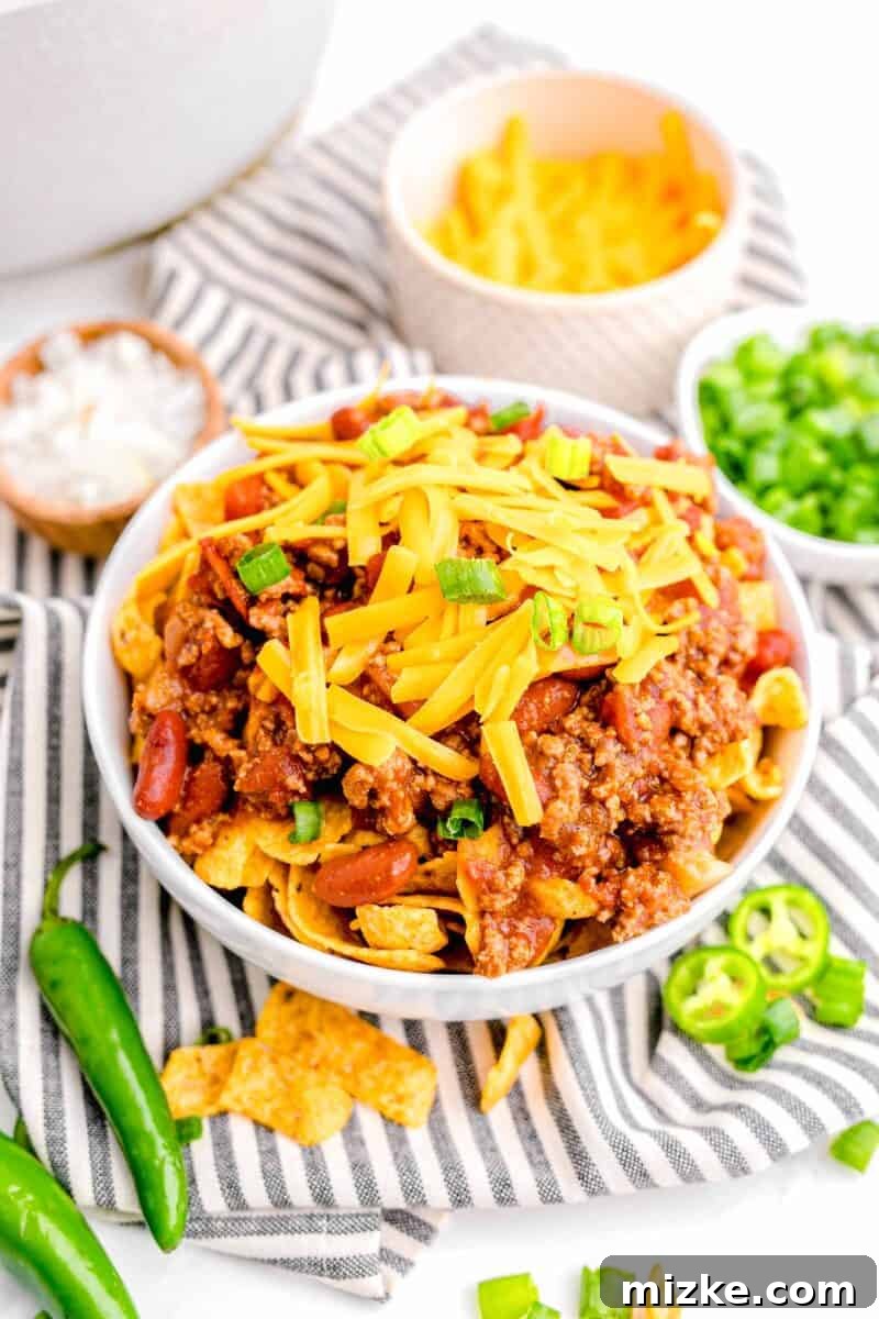 Ultimate Frito Chili Pie 11 A garnished bowl of frito chili pie is placed on a striped tea towel.