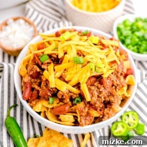 A garnished bowl of frito chili pie is placed on a striped tea towel.