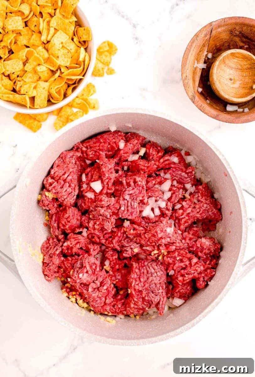 Ultimate Frito Chili Pie 4 Onions and garlic are added to a pot filled with uncooked beef.