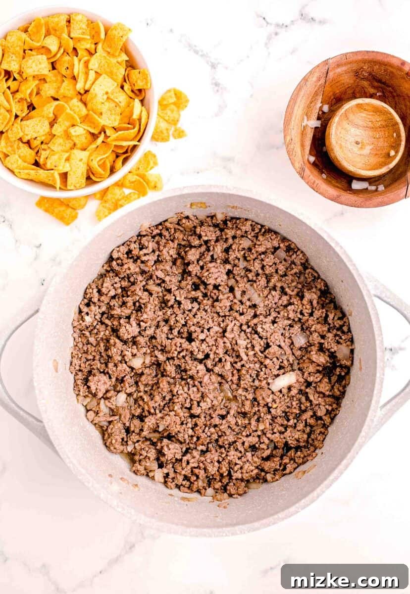Ultimate Frito Chili Pie 5 Cooked ground beef is presented in a white pot.