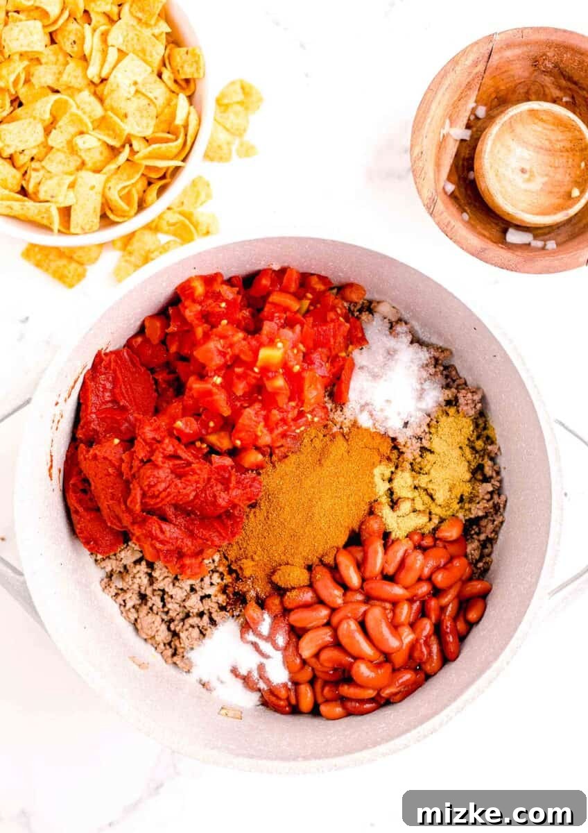Ultimate Frito Chili Pie 6 The ingredients for chili are placed in a white pot on top of cooked beef.