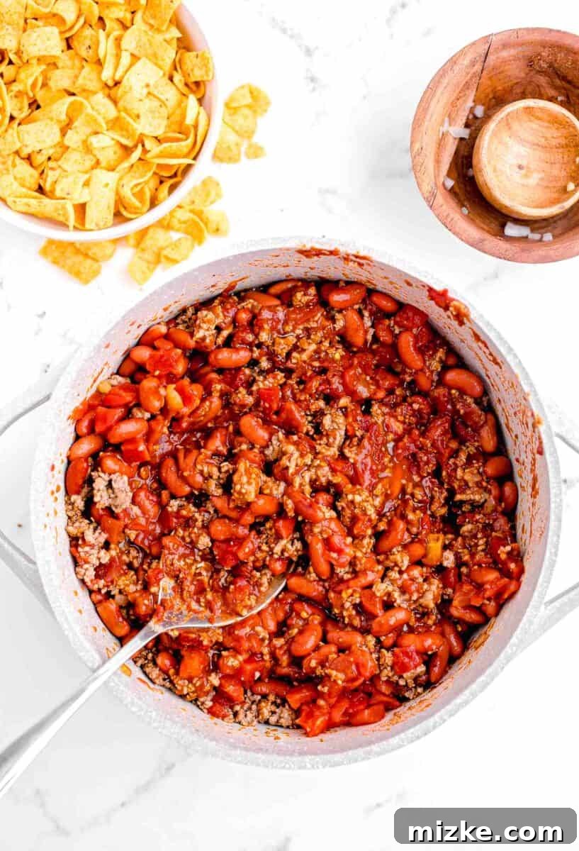 Ultimate Frito Chili Pie 7 Chili is being stirred together with a large spoon in a pot.