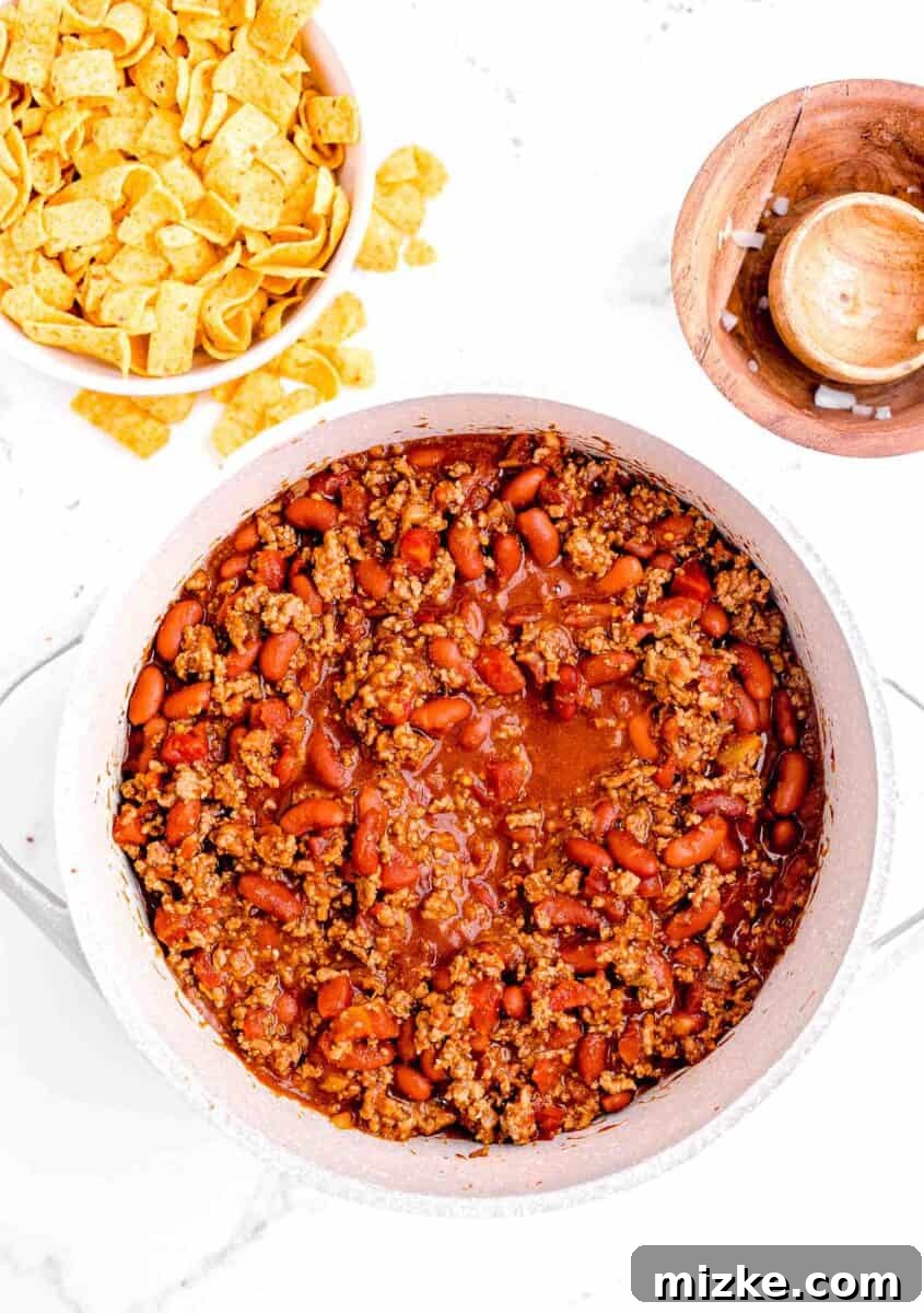 Ultimate Frito Chili Pie 8 Cooked chili is presented on a white surface next to a small white bowl filled with frots.