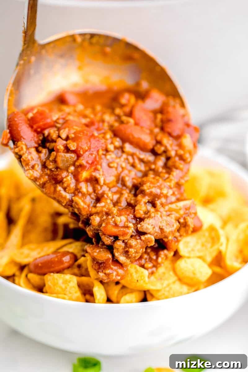 Ultimate Frito Chili Pie 9 Chili is being poured on top of a serving of fritos.