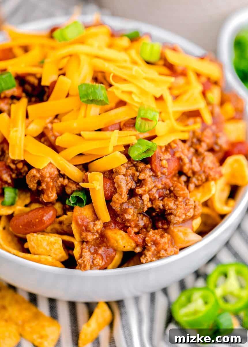 Ultimate Frito Chili Pie 10 A close up image shows the details of cheese, green onions, and chili on top of fritos in a bowl.