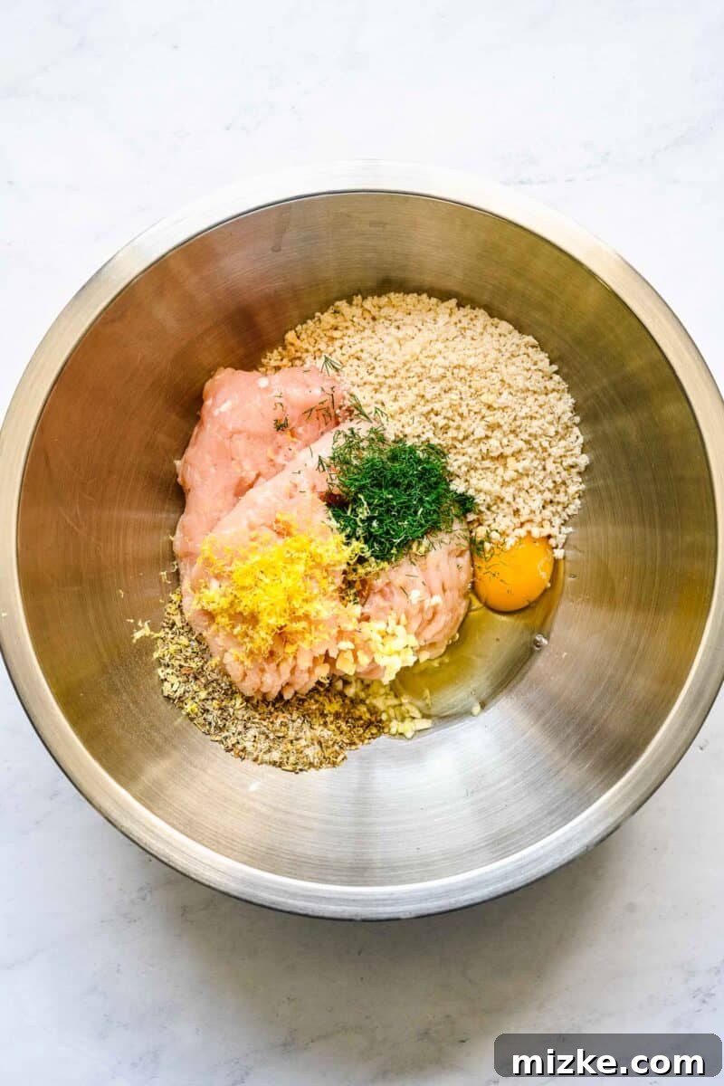 Zesty Greek Chicken Meatballs 4 All the Greek chicken meatball ingredients are gathered in a large silver mixing bowl, ready to be combined.
