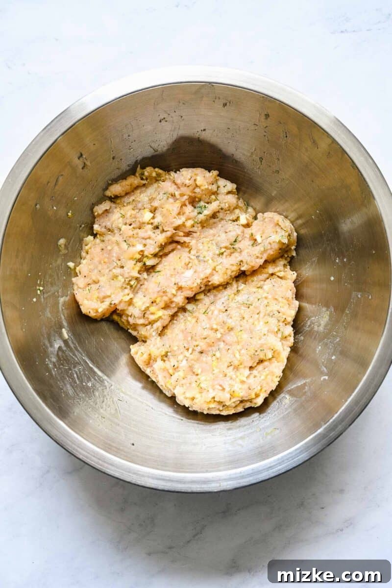 Zesty Greek Chicken Meatballs 5 The meatball ingredients have been thoroughly mixed together, forming a consistent and ready-to-shape mixture in the bowl.