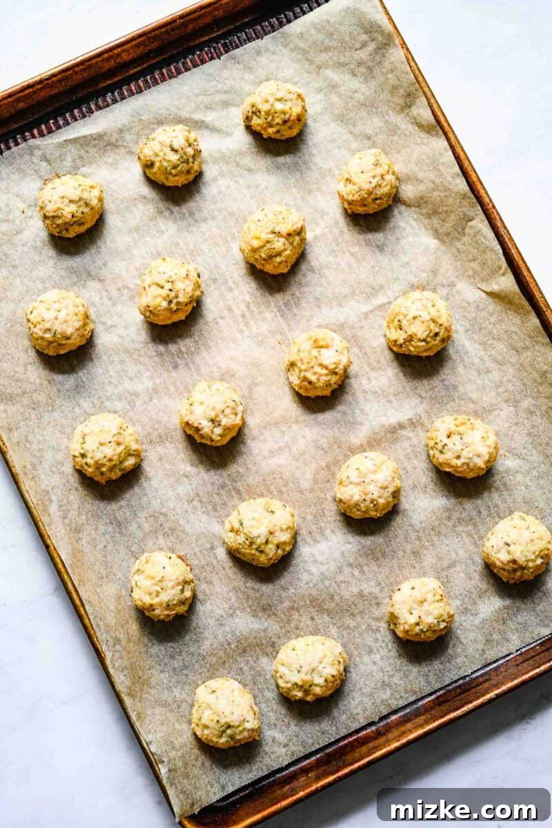 Zesty Greek Chicken Meatballs 6 Perfectly rolled Greek chicken meatballs neatly arranged on a parchment-lined baking sheet, spaced for even cooking.