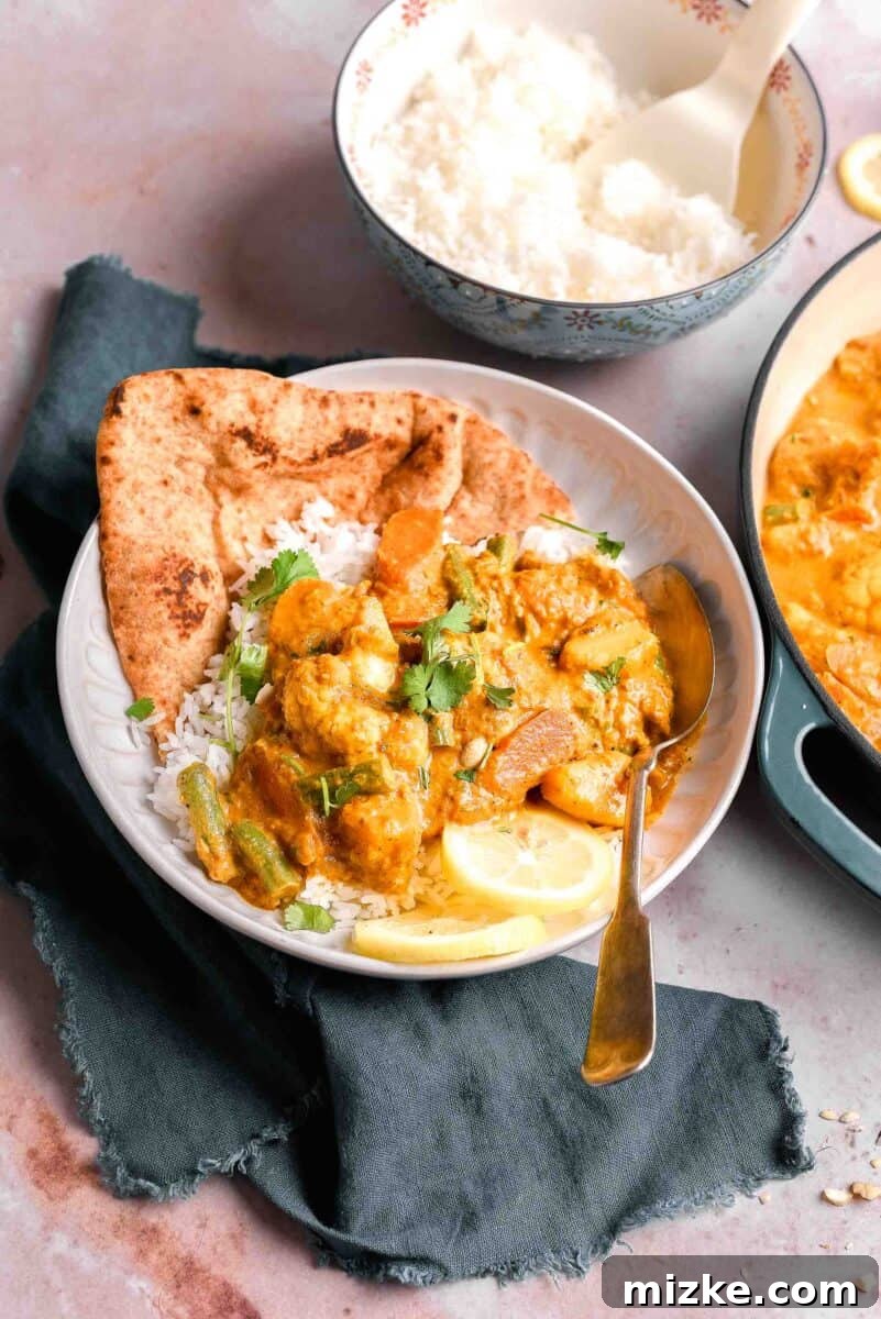 A single serving of vibrant vegetable korma presented elegantly on a white plate, garnished with fresh herbs, positioned alongside a rustic tea towel and a spoon, ready to be enjoyed.