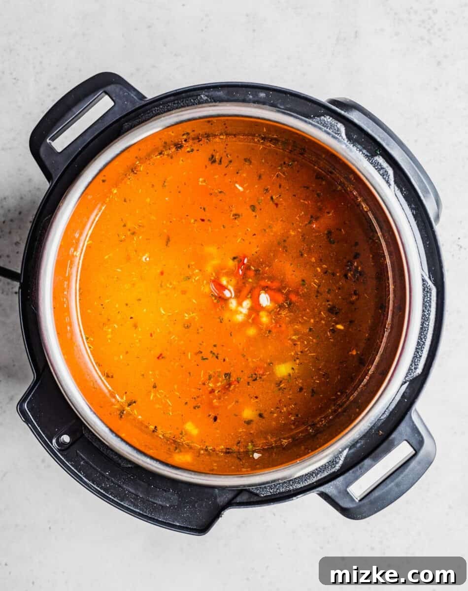 A rich, red broth with submerged beans and vegetables fills the Instant Pot, ready for pressure cooking.