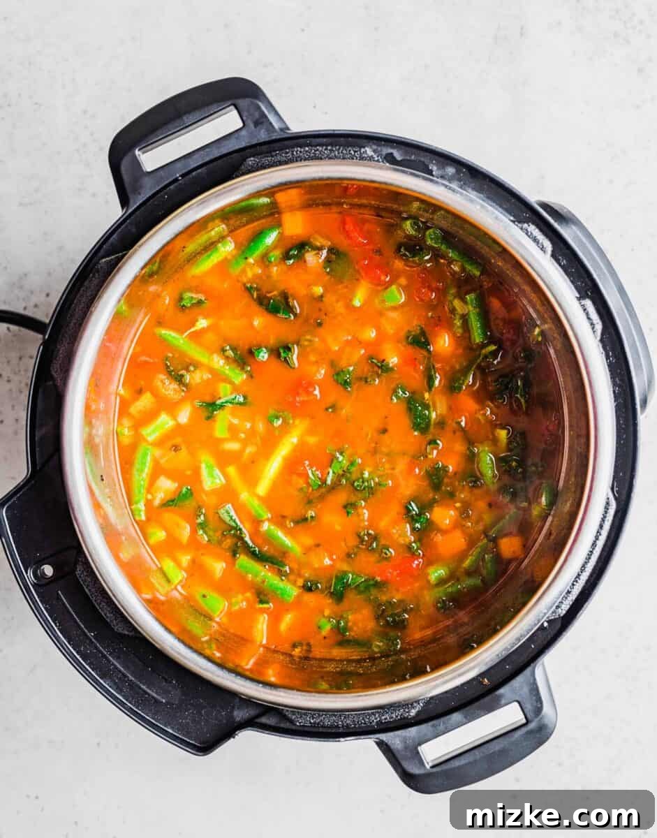 Fresh green vegetables, including kale and green beans, are stirred into the vibrant bean soup after pressure cooking.