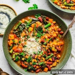 An overhead image shows the vibrant colors of the beans and vegetables in the soup. A spoon can be seen in the green bowl with the soup along with fresh grated parmesan on top.