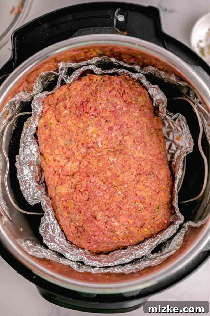 Perfect Instant Pot Meatloaf 6 An uncooked meatloaf, perfectly shaped and nestled within a makeshift foil loaf pan, is positioned inside the Instant Pot on a trivet, prepared for pressure cooking.