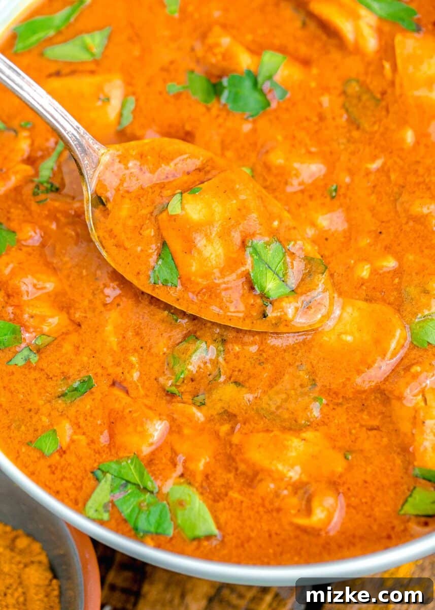 Effortless Crock-Pot Butter Chicken 3 A spoon lifting a generous portion of creamy slow cooker butter chicken from a serving bowl, highlighting its rich texture and tender chicken pieces.