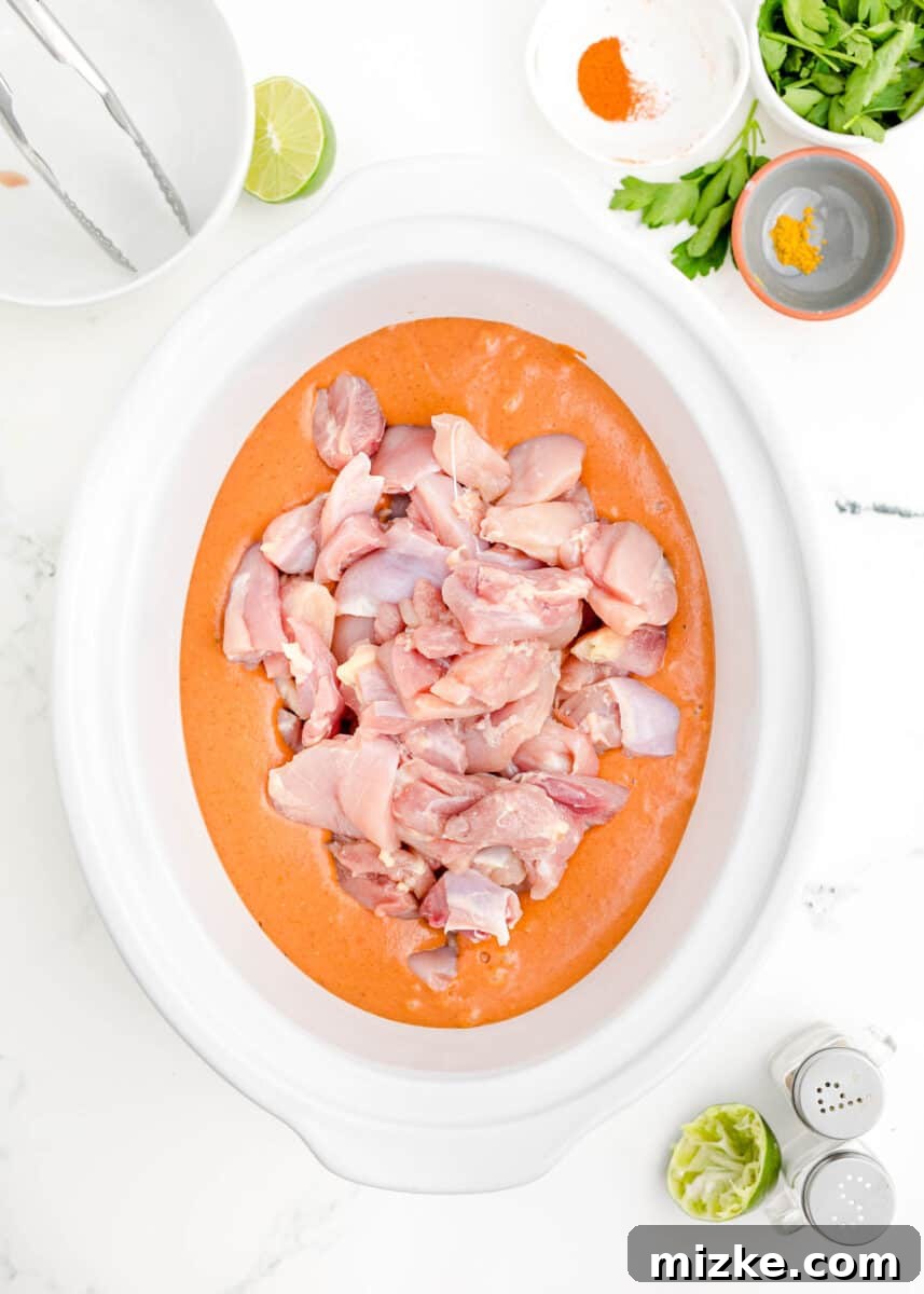 Effortless Crock-Pot Butter Chicken 7 Raw boneless, skinless chicken thighs placed evenly at the bottom of a slow cooker, meticulously arranged and ready to be fully coated with the rich butter chicken sauce.
