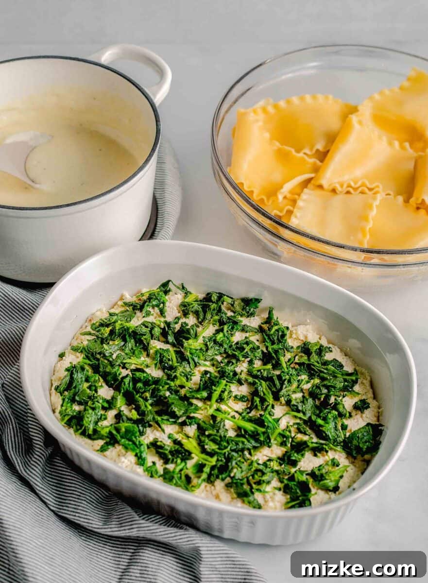 Fresh spinach leaves are spread out in a single, vibrant green layer within a casserole dish, adding a healthy component.