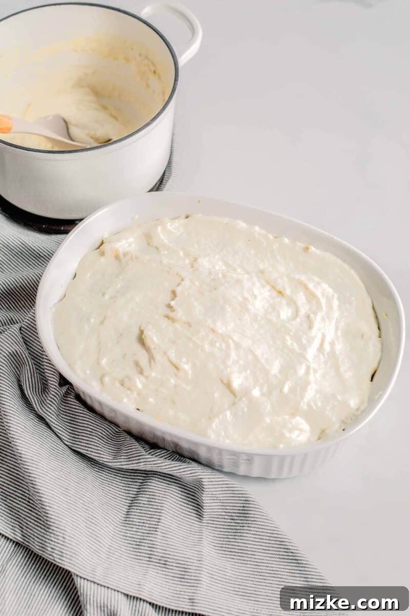 The final layer of creamy white sauce is spread generously over the top noodles of the lasagna before baking.