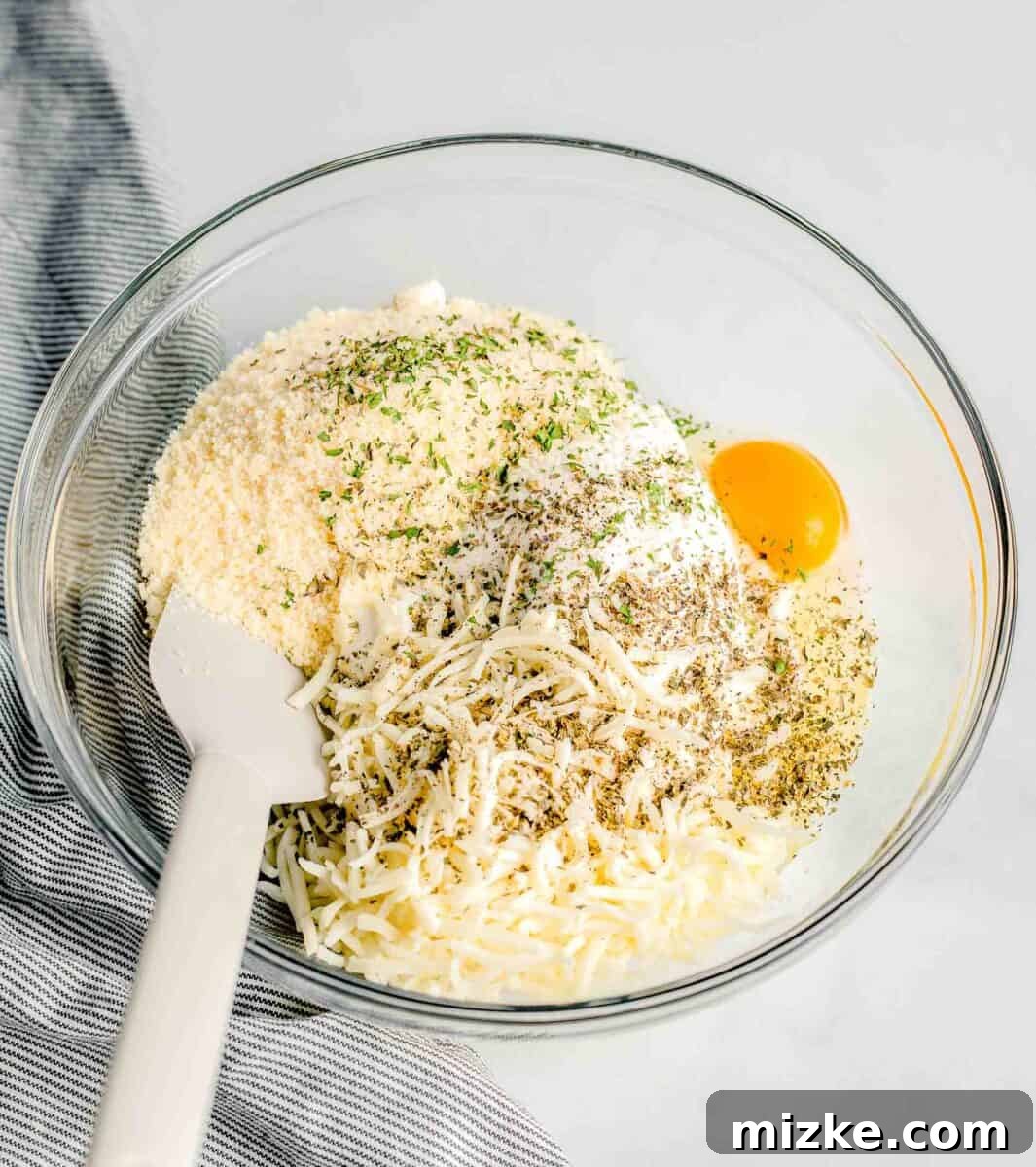 A glass mixing bowl holds ricotta cheese, egg, Parmesan, mozzarella, and dried herbs, ready to be combined for the chicken layer.