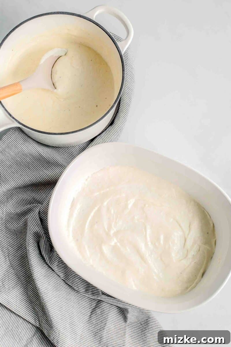 A thin layer of creamy white sauce is evenly spread across the bottom of a white casserole dish, providing a base for the lasagna.
