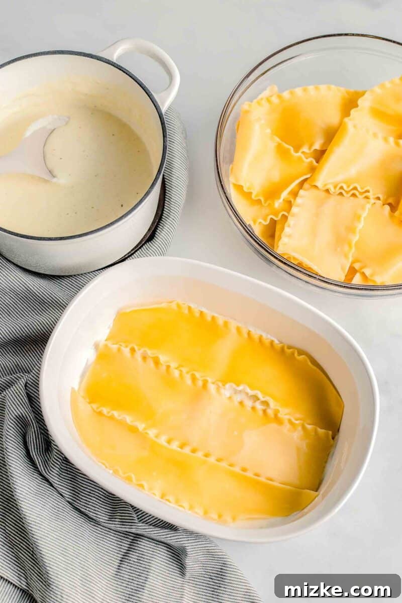 Cooked lasagna noodles are carefully arranged in a single, even layer at the bottom of a baking dish.