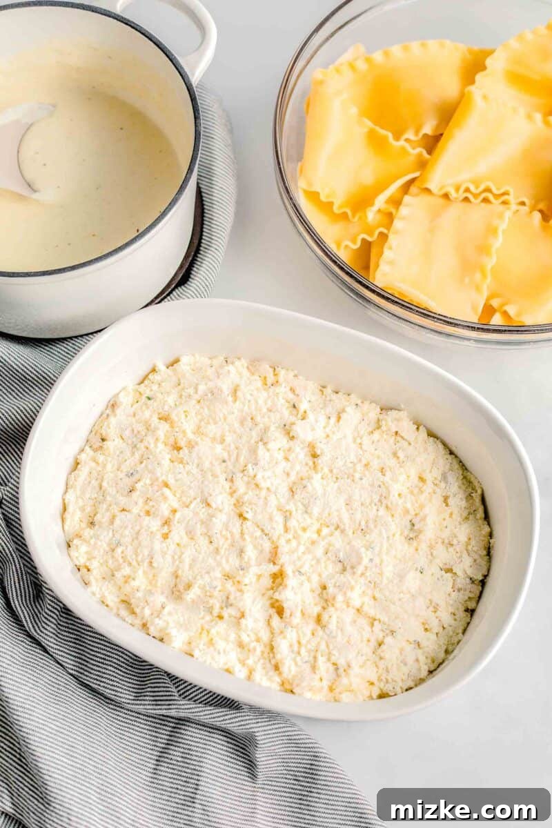 A white casserole dish sits beside containers of white sauce and cooked lasagna noodles, ready for assembly.