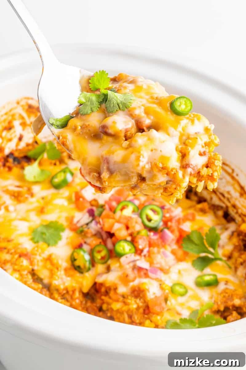 Slow Cooker Fiesta Quinoa Bake 2 A serving spoon lifts a portion of creamy, cheesy Slow Cooker Quinoa Enchilada Casserole from the Crockpot, revealing layers of quinoa and vegetables.