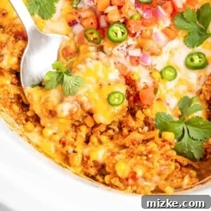 A large serving spoon is dipping into enchilada casserole.