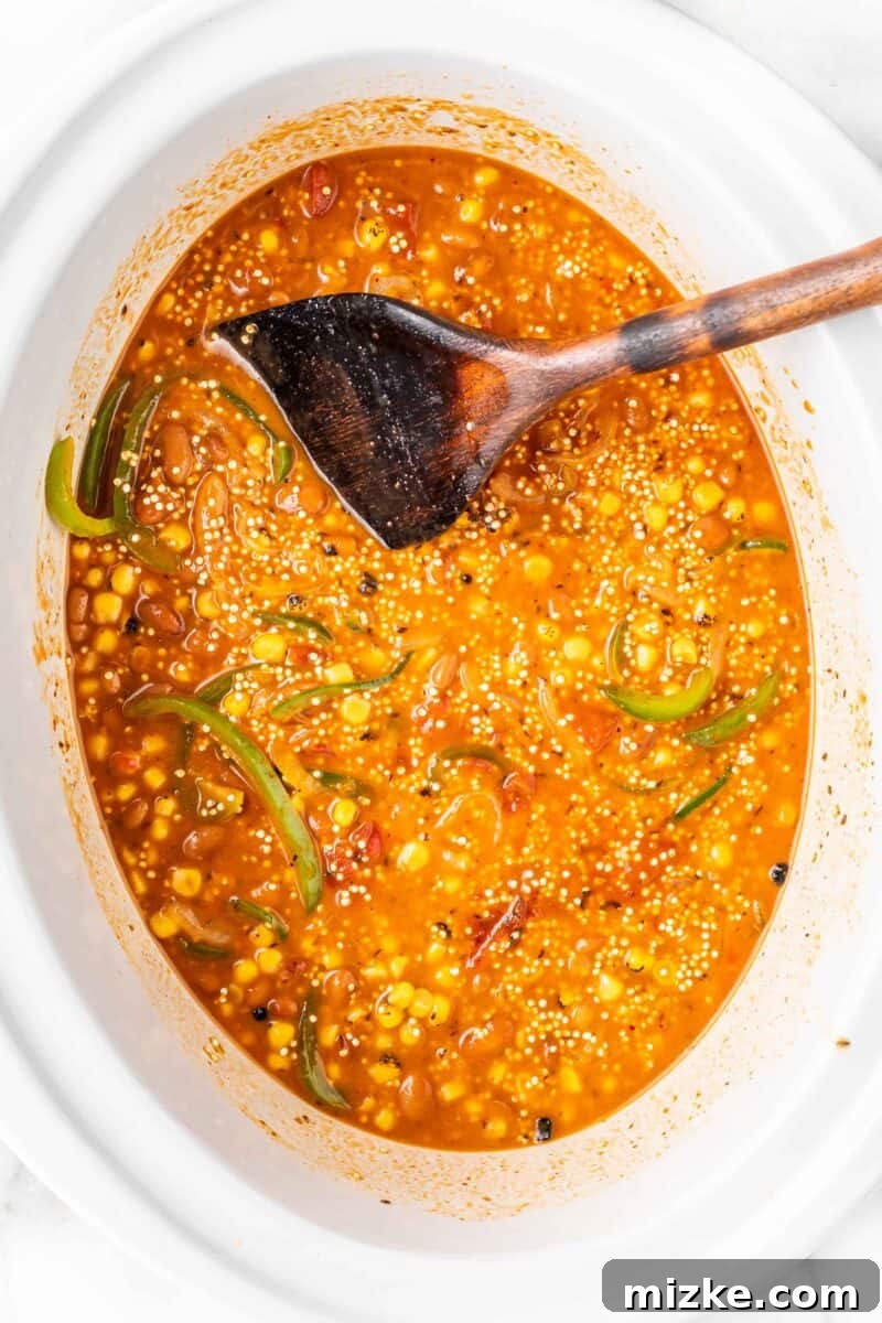 Slow Cooker Fiesta Quinoa Bake 7 A serving spoon is placed inside a Crockpot where the enchilada casserole is simmering, showing the rich, saucy texture of the cooking dish.