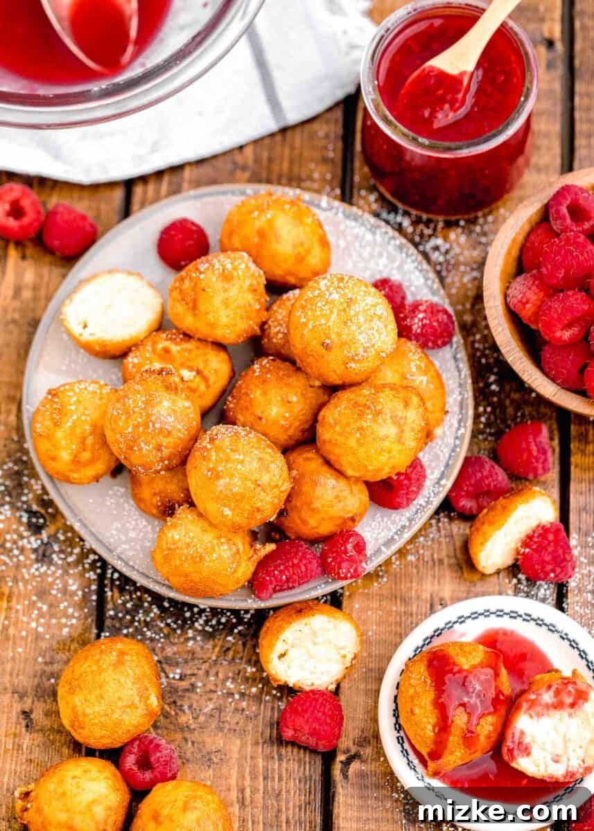Crispy Cheesecake Poppers 12 A rustic wooden plate is generously piled high with golden-brown fried cheesecake bites, artfully arranged with fresh, vibrant raspberries, ready for serving.