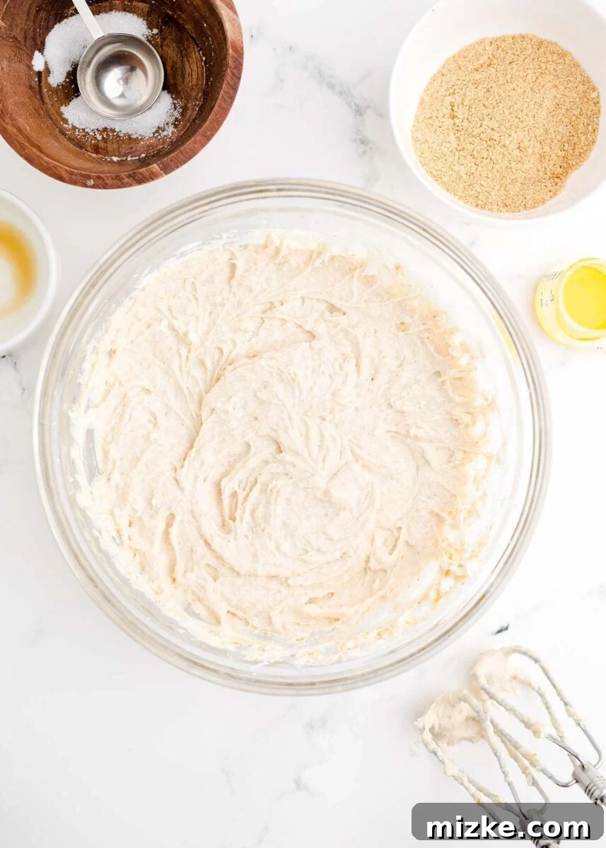 Crispy Cheesecake Poppers 5 A creamy, pale yellow cheesecake mixture is being thoroughly beaten with an electric hand mixer, ensuring a smooth and consistent texture.