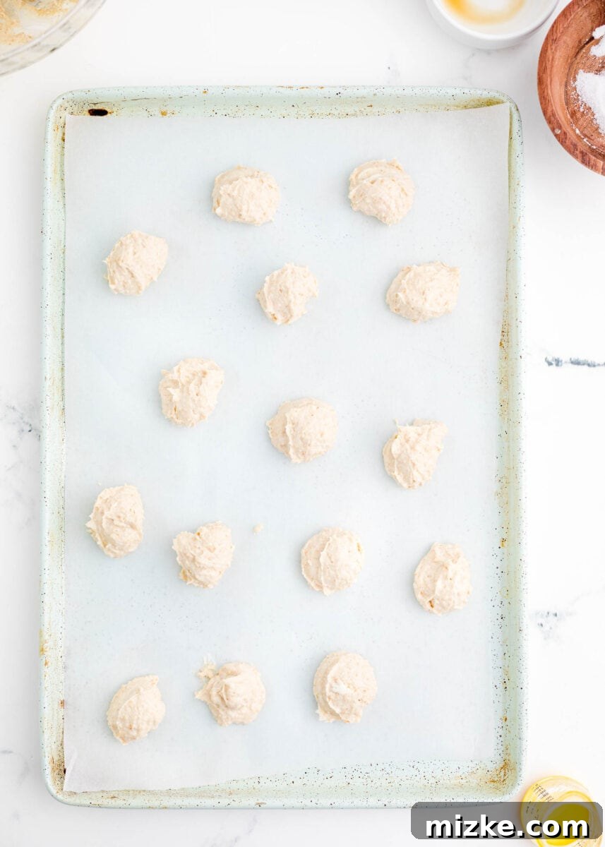Crispy Cheesecake Poppers 6 Multiple uniformly sized balls of white cream cheese mixture are neatly arranged on a parchment paper-lined baking sheet, ready for freezing.