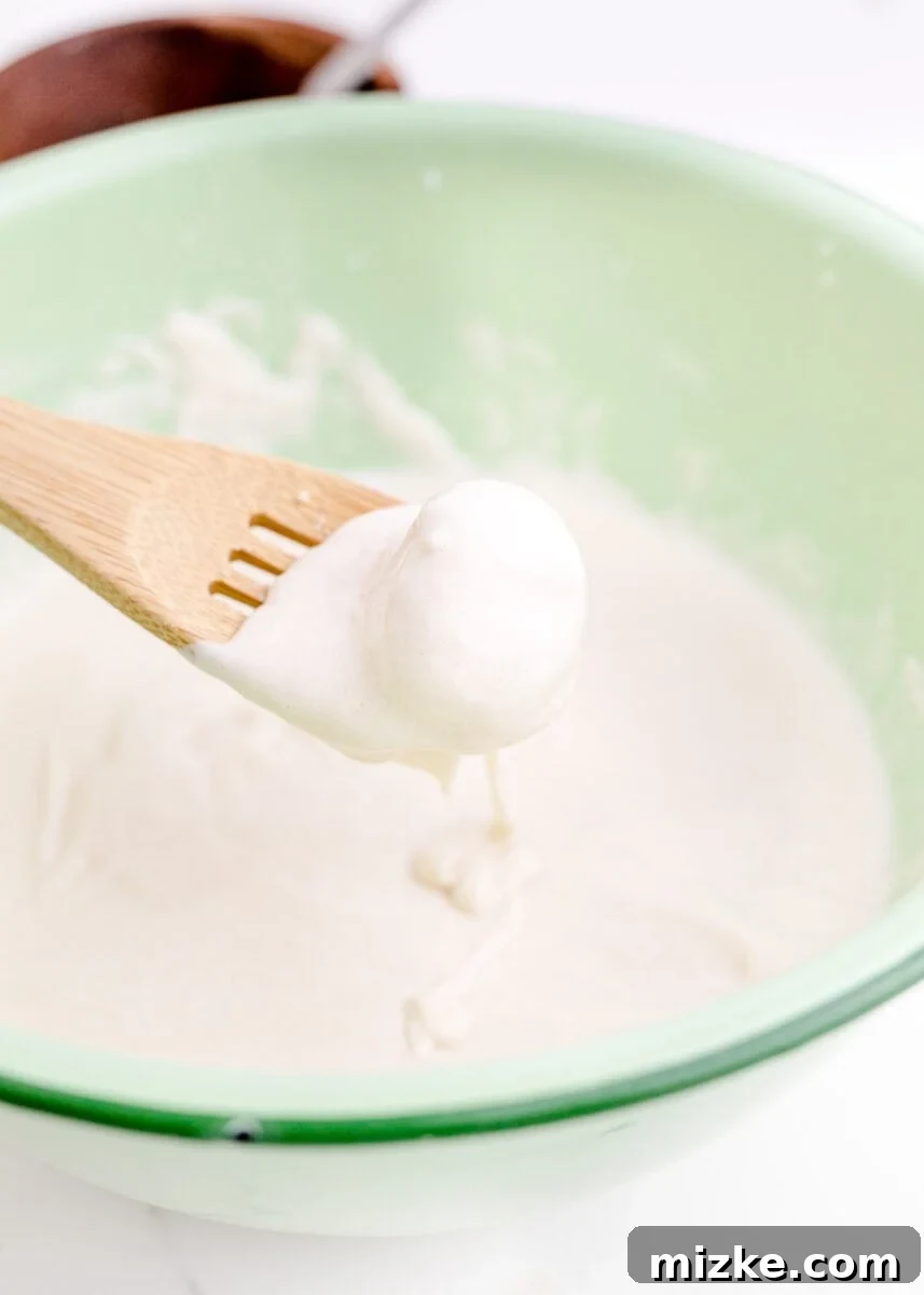 Crispy Cheesecake Poppers 8 A creamy, pale batter mixture is being gently stirred with a wooden spatula in a glass bowl, ensuring a consistent texture.