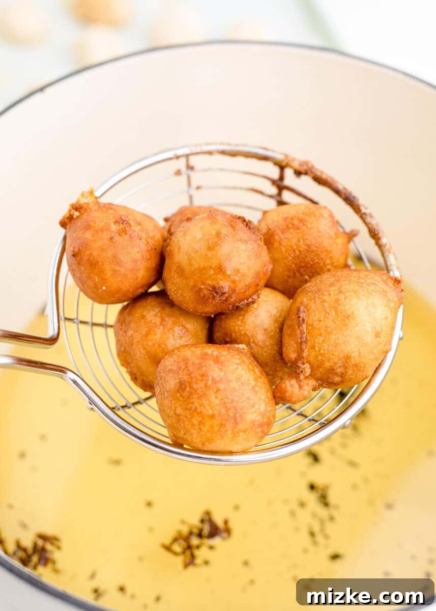 Crispy Cheesecake Poppers 9 Golden-brown fried cheesecake bites are carefully being lifted from a pot of shimmering hot oil with a slotted spoon, perfectly crisp.