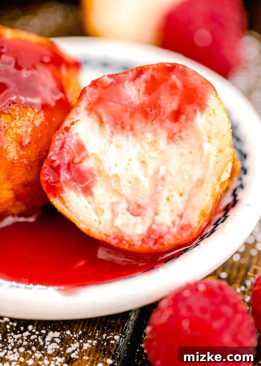 Crispy Cheesecake Poppers 10 A perfectly fried cheesecake bite with a soft, creamy interior is shown with a section bitten out, revealing its delicious texture, next to a dollop of vibrant raspberry sauce.