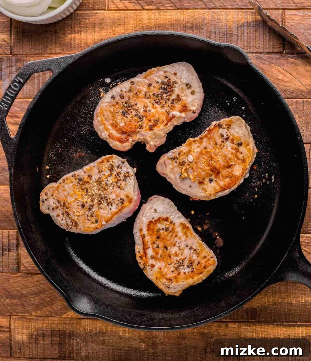 Flavorful Oven Roasted Pork Chops 4 Thick-cut pork chops sizzling and browning beautifully in a hot cast iron skillet, creating a perfect sear.