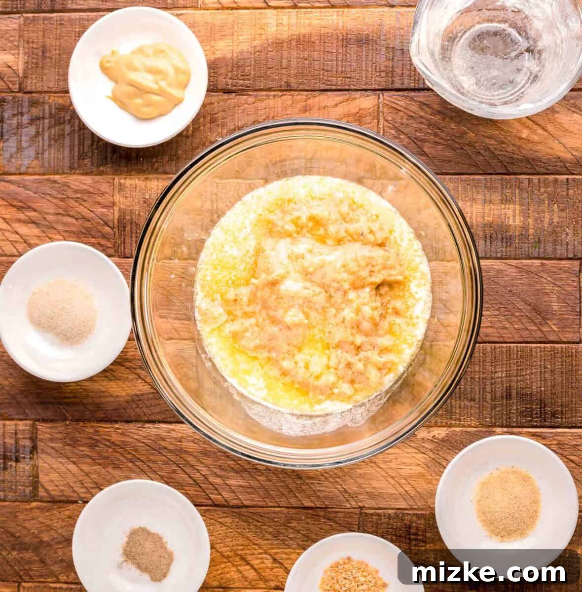 Flavorful Oven Roasted Pork Chops 6 Individual ingredients like melted butter, Dijon mustard, and various spices arranged in small white bowls, surrounding a larger glass bowl.