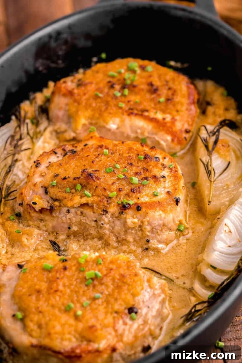 Juicy Oven-Roasted Pork Chops 10 Several beautifully roasted pork chops are elegantly presented in a baking pot, garnished with soft cooked onions and fresh herbs.