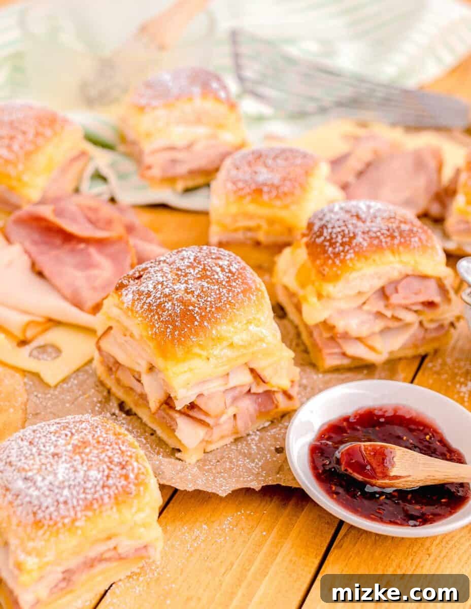 A small serving of jam is placed next to several golden-brown Monte Cristo Sliders on a rustic wooden board.