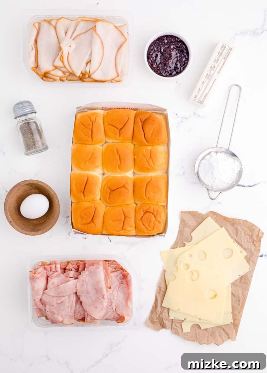 The fresh ingredients for Monte Cristo Sliders, including Hawaiian rolls, deli meats, Swiss cheese, and butter, are neatly presented on a pristine white surface.