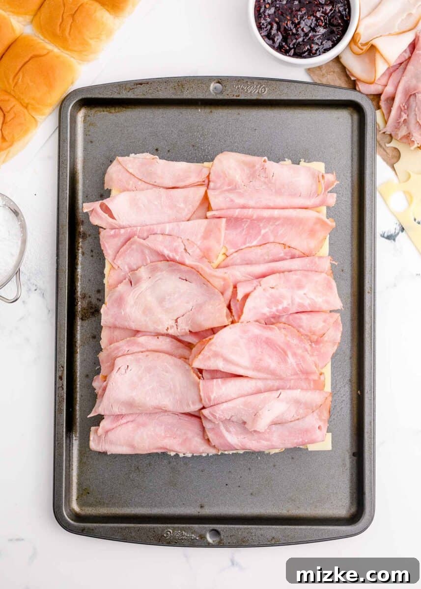 A perfectly layered sheet of deli ham is visible within a baking dish, ready for the next ingredient.