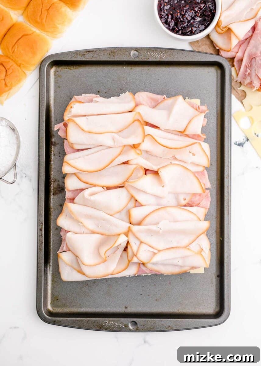 A layer of thinly sliced deli turkey is carefully placed over the ham, forming the next delicious layer in the baking sheet.