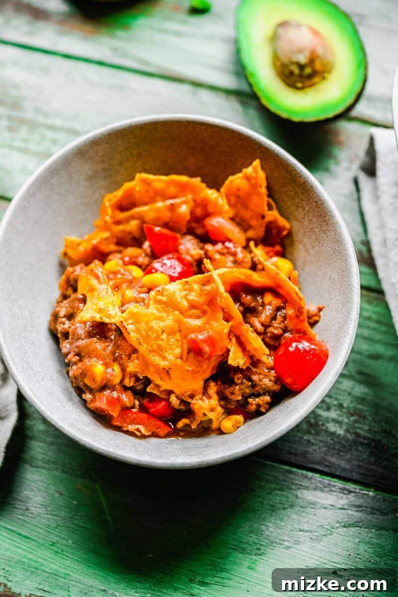 A delicious individual portion of taco casserole, ready to be customized with avocado. A single serving of taco casserole presented in a small bowl, with a perfectly ripe avocado positioned next to it, suggesting fresh toppings.