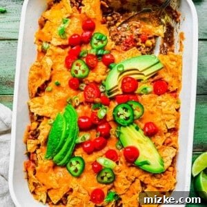 A spoon scooping a generous portion of cheesy, layered taco casserole from a white baking dish, garnished with fresh toppings like avocado and jalapeños.