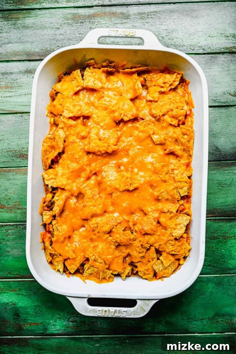 The perfectly baked taco casserole with melted, browned cheese. The finished taco casserole, fresh from the oven, features golden-brown melted cheese atop crushed tortilla chips in a white baking dish, presented on a green background.