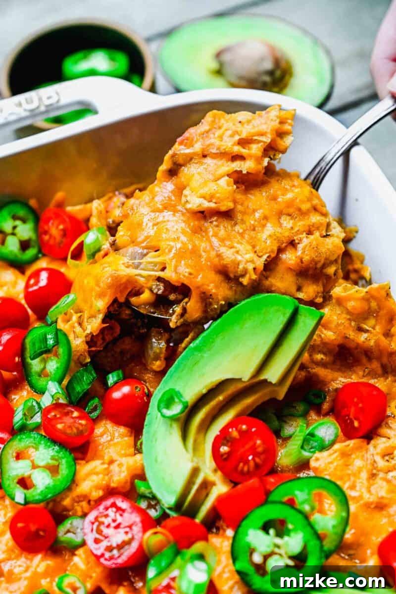 Scooping up a satisfying serving of homemade taco casserole. A serving spoon plunges into the warm, cheesy taco casserole, revealing its delicious layers of ground beef, beans, and chips, ready to be enjoyed.