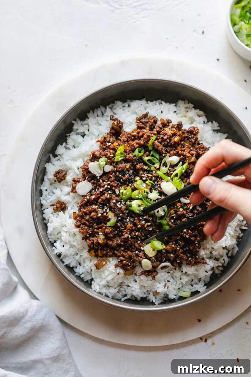 Sizzling Korean Beef Delights 5 A person mixing Korean Ground Beef with perfectly cooked rice noodles and the savory sauce in a large pan, demonstrating a delicious and versatile serving option beyond traditional rice.