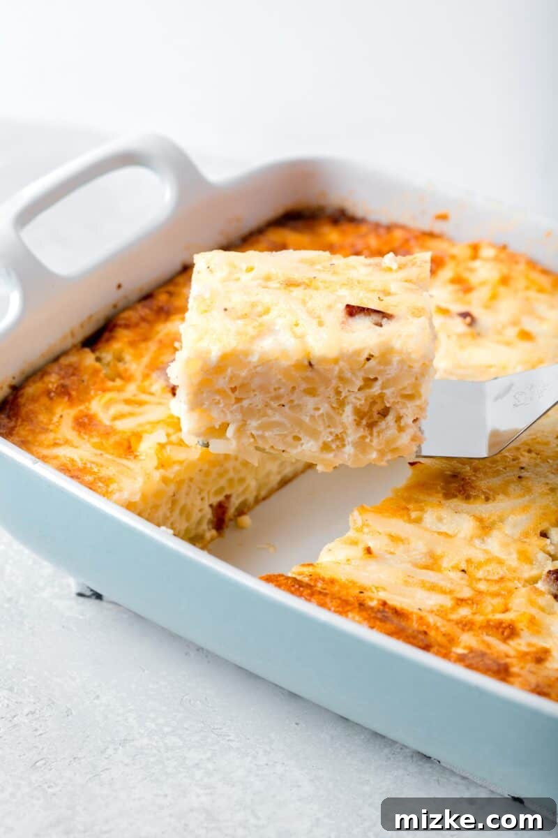 A perfectly golden slice of egg white breakfast casserole being lifted from a baking dish with a metal spatula, showcasing its fluffy texture and savory ingredients, ready to be served.